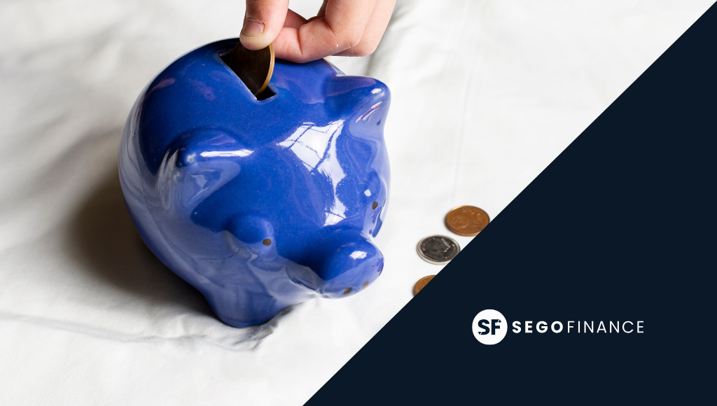 Mano introduciendo moneda en hucha azul, concepto de ahorro e inversión en SEGOFINANCE