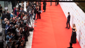 Fotógrafos y medios captando imágenes en una alfombra roja mientras dos personas posan frente al photocall.