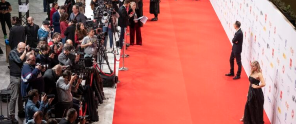 Fotógrafos y medios captando imágenes en una alfombra roja mientras dos personas posan frente al photocall.