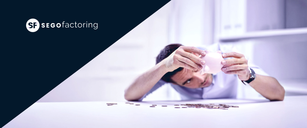 Empresario sacudiendo una hucha vacía sobre una mesa con monedas sueltas, ilustrando los problemas de liquidez de las pymes, con el logo de SEGO Factoring