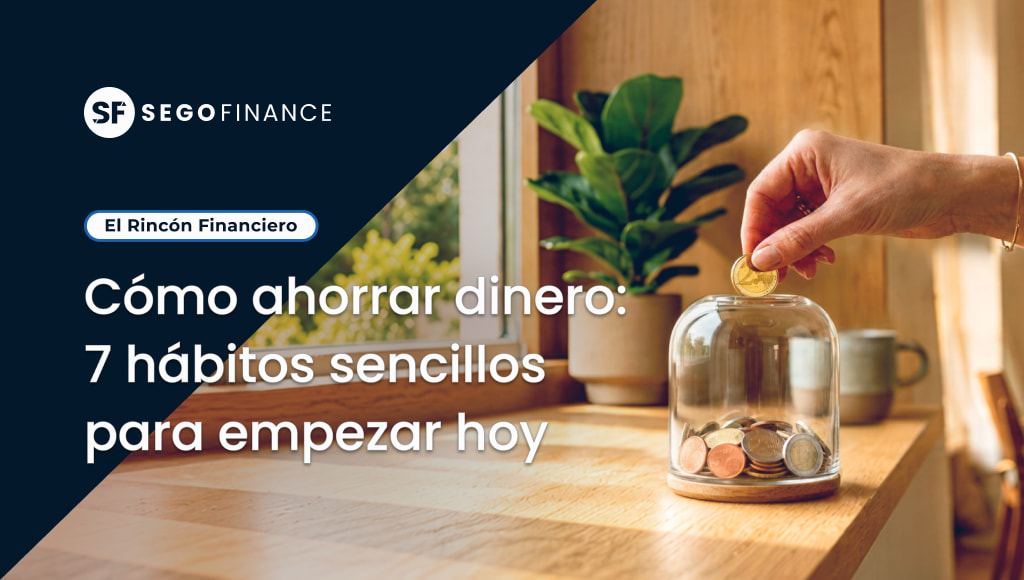 Mano introduciendo una moneda en un tarro de cristal con ahorros sobre una mesa de madera junto a una ventana
